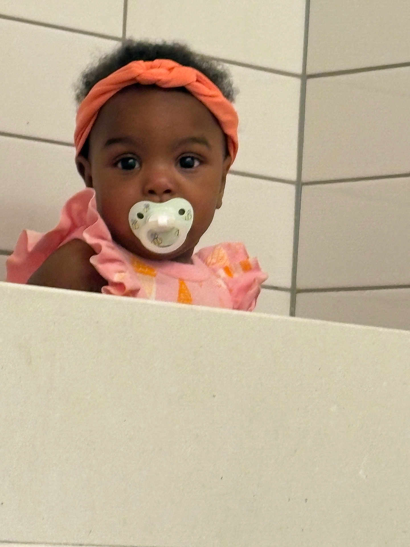 Amani joined the competition — help win amazing prizes! toddler, child, pacifier, headband, pink_clothing, curly_hair, face, portrait, indoor, tile_wall, ledgeline, baby, cute, looking, young_child, person, infant, expression, fashion, closeup