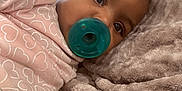 Amani joined the competition — help win amazing prizes! baby, pacifier, pink_clothing, heart_pattern, blanket, plush, close_up, indoor, child, infant, cute, resting, soft_texture, face, eyes, skin, comfort, cozy, window_light, toddler