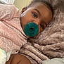 baby, pacifier, pink_clothing, heart_pattern, blanket, plush, close_up, indoor, child, infant, cute, resting, soft_texture, face, eyes, skin, comfort, cozy, window_light, toddler