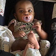 Amani is registered to the contest to win money with this photo: baby, pacifier, car_seat, blanket, bottle, infant, child, cute, clothing, foot, hand, lying_down, indoors, soft, portrait, resting, young, childcare, baby_girl, comfort