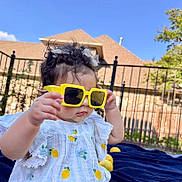 Anaiah is registered to the contest to win money with this photo: toddler, child, baby, yellow_sunglasses, curly_hair, white_dress, lemon_pattern, outdoor, blue_sky, fence, house, blanket, playful, sunny, summer, portrait, cute, childhood, fashion, fun