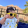 toddler, child, baby, yellow_sunglasses, curly_hair, white_dress, lemon_pattern, outdoor, blue_sky, fence, house, blanket, playful, sunny, summer, portrait, cute, childhood, fashion, fun
