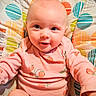 baby, infant, child, smiling, portrait, strawberry_outfit, pink_clothing, baby_seat, cushion, colorful, patterned, indoor, close_up, face, eyes, happy, sitting, photography, nursery, cute