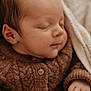 baby, sleeping, knitted_sweater, brown_clothing, blanket, cozy, infant, peaceful, close_up, soft_light, portrait, newborn, cute, warm, child, face, hand, indoor, relaxation, comfort