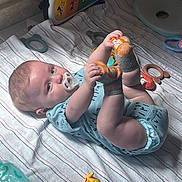 Joshua is registered to the contest to win money with this photo: baby, infant, child, lying_down, smiling, pacifier, sock, feet, hands, onesie, bed, blanket, striped_bedding, toys, rattle, teether, musical_toy, nursery, indoor, portrait