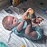baby, infant, child, lying_down, smiling, pacifier, sock, feet, hands, onesie, bed, blanket, striped_bedding, toys, rattle, teether, musical_toy, nursery, indoor, portrait