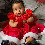 Yunuen is registered to the contest to win money with this photo: baby, child, smiling, red_dress, black_shoes, bed, blanket, pillow, indoors, cute, holiday, festive, infant, person, portrait, sitting, happy, clothing, face, hair