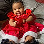 baby, child, smiling, red_dress, black_shoes, bed, blanket, pillow, indoors, cute, holiday, festive, infant, person, portrait, sitting, happy, clothing, face, hair