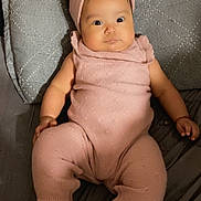 Yunuen is registered to the contest to win money with this photo: baby, infant, pink_outfit, headband, white_shoes, quilted_cushion, gray_bedspread, lying_down, wide_eyes, curious_expression, knitted_clothing, chubby_cheeks, indoor, cute, child, adorable, soft_lighting, portrait, person, toddler