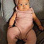 baby, infant, pink_outfit, headband, white_shoes, quilted_cushion, gray_bedspread, lying_down, wide_eyes, curious_expression, knitted_clothing, chubby_cheeks, indoor, cute, child, adorable, soft_lighting, portrait, person, toddler