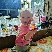 Lyric joined the competition — help win amazing prizes! bedspread, candy, child, clutter, face, fan, floral_pattern, food_smear, indoor, kitchen_window, mess, monitor, pink_sweater, plastic_container, shoe, smile, sock, soda_bottle, toddler, window