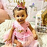 baby, child, toddler, birthday, crown, pink_dress, smiling, sitting, portrait, indoors, party, balloons, birthday_decorations, blanket, stuffed_animal, bedroom, dress, infant, celebration, photography