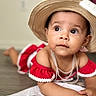 Aliana is registered to the contest to win money with this photo: baby, child, hat, straw_hat, red_clothing, off_shoulder, earrings, necklace, floor, towel, indoor, portrait, cute, curious, lying_down, closeup, face, skin, eyes, expression