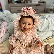 Aliana is registered to the contest to win money with this photo: baby, child, smile, happy, dress, lace, headpiece, pink, cute, sitting, indoors, blanket, foot, portrait, infant, clothing, face, person, young_child, cozy