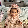 baby, child, smile, happy, dress, lace, headpiece, pink, cute, sitting, indoors, blanket, foot, portrait, infant, clothing, face, person, young_child, cozy