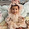 baby, child, dress, lace, bonnet, pink, smile, face, sitting, bed, blanket, pillow, indoors, person, clothing, cute, happy, infant, portrait, home