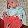 baby, infant, smile, red_pants, blue_sweater, lying_down, pillow, patterned_pillow, foot, hand, cute, cheeky, indoors, child, person, cozy, happy, small, young, casual_clothing