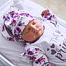 newborn, baby, sleeping, crib, hat, floral_pattern, white_clothing, infant, cute, peaceful, indoors, portrait, child, soft_light, resting, small_hands, cute_outfit, baby_girl, cozy, toddler