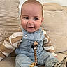 Lyandro participe au concours pour gagner de l'argent avec cette photo : baby, smiling, child, denim_overalls, striped_sweater, sneakers, pacifier_clip, couch, beige, indoor, cute, portrait, seated, happy, young_child, face, clothing, person, infant, casual