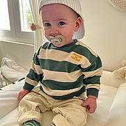 Lyandro participe au concours pour gagner de l'argent avec cette photo : toddler, child, pacifier, cap, striped_sweater, beige_pants, striped_socks, indoor, couch, window, natural_light, curtains, baby, cute, smiling, person, seated, soft_lighting, casual_clothing, portrait