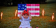 Milani joined the competition — help win amazing prizes! toddler, child, grass, outdoor, fireworks, red_bow, american_flag, hand_painted, patriotic, celebration, summer, toy_shoes, white_dress, nature, festive, holiday, sparkler, smiling, portrait, sitting