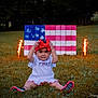 toddler, child, grass, outdoor, fireworks, red_bow, american_flag, hand_painted, patriotic, celebration, summer, toy_shoes, white_dress, nature, festive, holiday, sparkler, smiling, portrait, sitting