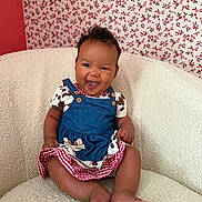 Naomi is registered to the contest to win money with this photo: baby, blue_dress, child, couch, cow_print, cream_couch, cute, dress, feet, floral_wallpaper, happy, indoor, infant, person, portrait, red_gingham, sitting, smiling, textured_fabric, wallpaper