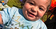 Zakai joined the competition — help win amazing prizes! toddler, child, smiling, curly_hair, blue_shirt, outdoor, grass, sunny, backyard, fence, person, blanket, bag, playing, happy, casual_clothing, daylight, portrait, closeup, fun