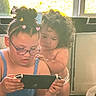 Zakai joined the competition — help win amazing prizes! child, baby, glasses, hair_clips, curly_hair, playing, game_console, indoor, window, sibling, bonding, shirtless, diaper, focus, curiosity, home, couch, netting, floor, hands