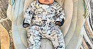 Ayden is registered to the contest to win money with this photo: baby, infant, baby_seat, plush_toy, sun_plush, onesie, dog_prints, carpet, patterned_rug, floor, indoors, child, cute, portrait, soft_cushion, head_support, clothing, person, comfort, home