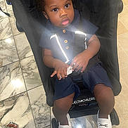Tishawn joined the competition — help win amazing prizes! toddler, child, stroller, navy_outfit, white_shoes, reflective_strips, marble_floor, hands, curly_hair, indoor, floor_tiles, footwear, person, infant, baby, seatbelt, black_stroller, looking_up, holding_object, cute