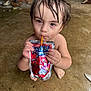 child, toddler, wet_hair, drink, juice_pouch, concrete_floor, barefoot, curious, cherry_flavor, sitting, crouching, face, person, refreshment, thirsty, young_child, indoor, close_up, portrait, hands