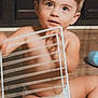 toddler, child, diaper, indoor, floor, wooden_floor, metal_rack, blue_cup, curious, sitting, baby, cabinet, light_skin, short_hair, playful, bare_chest, hand, foot, expression, young_child