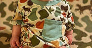 Oakley is registered to the contest to win money with this photo: adorable, baby, barefoot, blanket, bow_headband, camouflage, child, colorful, face, green, indoors, infant, outfit, pacifier, patterned, photography, portrait, sitting, toes, wide_eyes