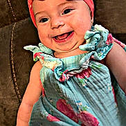 Oakley is registered to the contest to win money with this photo: baby, child, infant, smiling, happy, portrait, indoors, chair, seated, pink_bow, headband, floral_dress, colorful_clothing, face, eyes, open_mouth, teeth, cheeks, couch, closeup