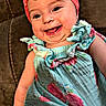 baby, child, infant, smiling, happy, portrait, indoors, chair, seated, pink_bow, headband, floral_dress, colorful_clothing, face, eyes, open_mouth, teeth, cheeks, couch, closeup