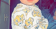 Oakley is registered to the contest to win money with this photo: baby, child, infant, portrait, bow, yellow_bow, blue_eyes, wide_eyed, sitting, onesie, cartoon_print, lion_print, clothing, adult, hand, tattoo, indoors, bedroom, shelf, family_photo