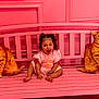 toddler, child, pink_bench, pink_wall, plush_cat, cat_cushion, pigtails, smiling, happy, sitting, indoor, decorative_molding, childrens_clothing, toy, cute, playful, bright_colors, portrait, childhood, fun