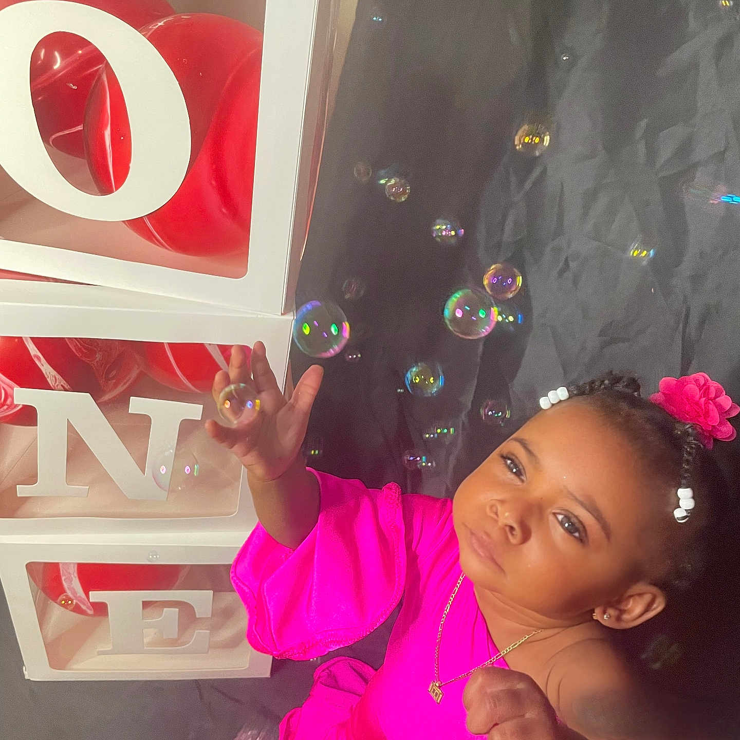 Haelie is registered to the contest to win money with this photo: accessories, baby_girl, beads, black_background, bracelet, bubbles, celebration, child, curious, cute, decor, happy, indoor, love_blocks, necklace, pink_clothing, playing, portrait, red_balloons, toddler