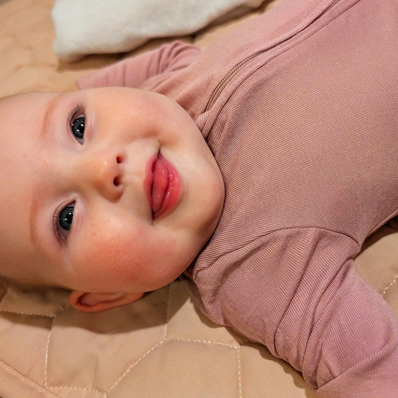 Luna joined the competition — help win amazing prizes! baby, infant, face, tongue, expression, cute, child, lying_down, mauve_clothing, quilted_mat, skin, cheeks, eyes, person, soft_texture, comfort, happy, indoors, portrait, closeup