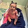 baby, child, infant, pink_clothing, baby_seat, blanket, water_bottle, tongue_out, indoor, floor_mat, green_wall, cabinet, hair_ties, cute, playful, sitting, person, portrait, expression, home