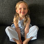 Ava Belle is registered to the contest to win money with this photo: child, smiling, blonde_hair, blue_outfit, striped_clothing, sitting, couch, indoor, happy, portrait, cute, young_child, person, face, barefoot, long_hair, casual, home, light, relaxed