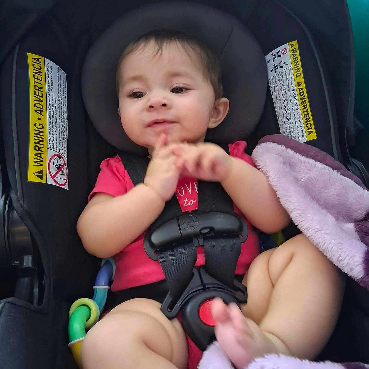 Ellie joined the competition — help win amazing prizes! baby, car_seat, child, pink_clothing, blanket, toy, clapping, infant, seatbelt, cute, indoors, safety, happy, face, hands, legs, foot, expression, comfort, car