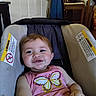 baby, child, car_seat, pink_clothing, butterfly, smiling, indoor, door, chair, household, seat, infant, person, cute, happy, young_child, casual, comfort, small_child, portrait