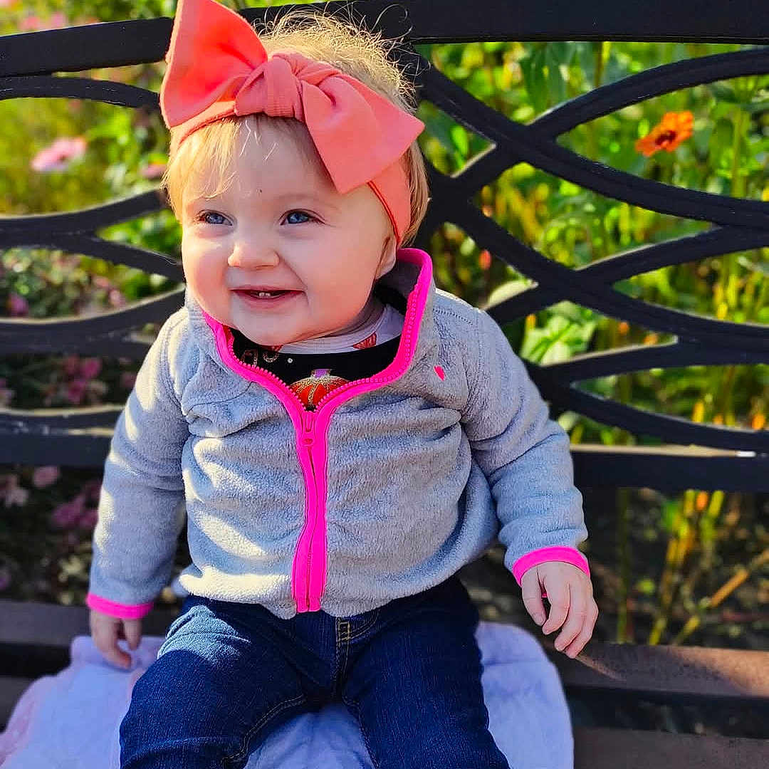 Ryla-Mae joined the competition — help win amazing prizes! baby, bench, clothing, coat, face, furniture, grass, happy, head, jacket, jeans, pants, person, photography, plant, portrait, pottedplant, sitting, sleeve, smile