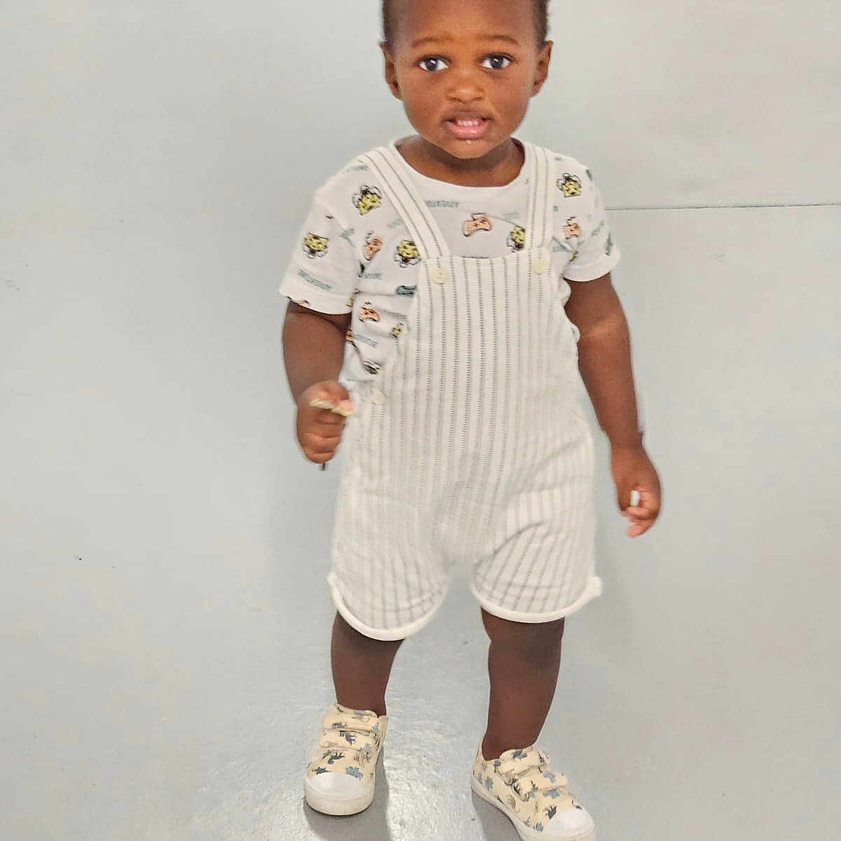 Hakeem a rejoint le concours — aidez-le/la à gagner de superbes lots ! baby, child, clothing, curious, cute, expression, fashion, floor, footwear, indoor, kid, overalls, person, portrait, shirt, shoes, sneakers, standing, toddler, young_child