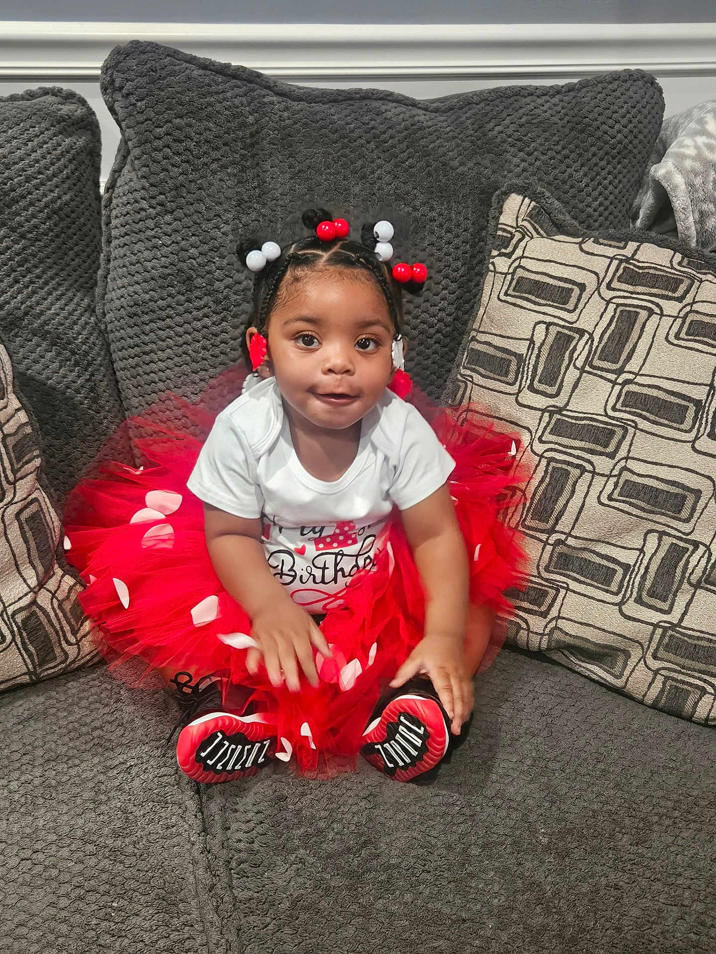 Alasia is registered to the contest to win money with this photo: child, toddler, birthday, red_tutu, white_shirt, sitting, couch, pillows, patterned_pillows, beaded_hair, indoor, smiling, happy, cute, celebration, person, young_child, fashion, home, portrait