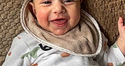Adan a rejoint le concours — aidez-le/la à gagner de superbes lots ! baby, smiling, onesie, heart_pattern, bib, blanket, happy, infant, cute, face, child, lying_down, cozy, texture, comfort, indoors, skin, head, expression, young