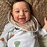 baby, smiling, onesie, heart_pattern, bib, blanket, happy, infant, cute, face, child, lying_down, cozy, texture, comfort, indoors, skin, head, expression, young