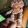 baby, infant, pink_pajamas, bonnet, smiling, tongue_out, person, legs, hand, tablet, screen, indoor, bed, blanket, furniture, home, cute, happy, child, portrait